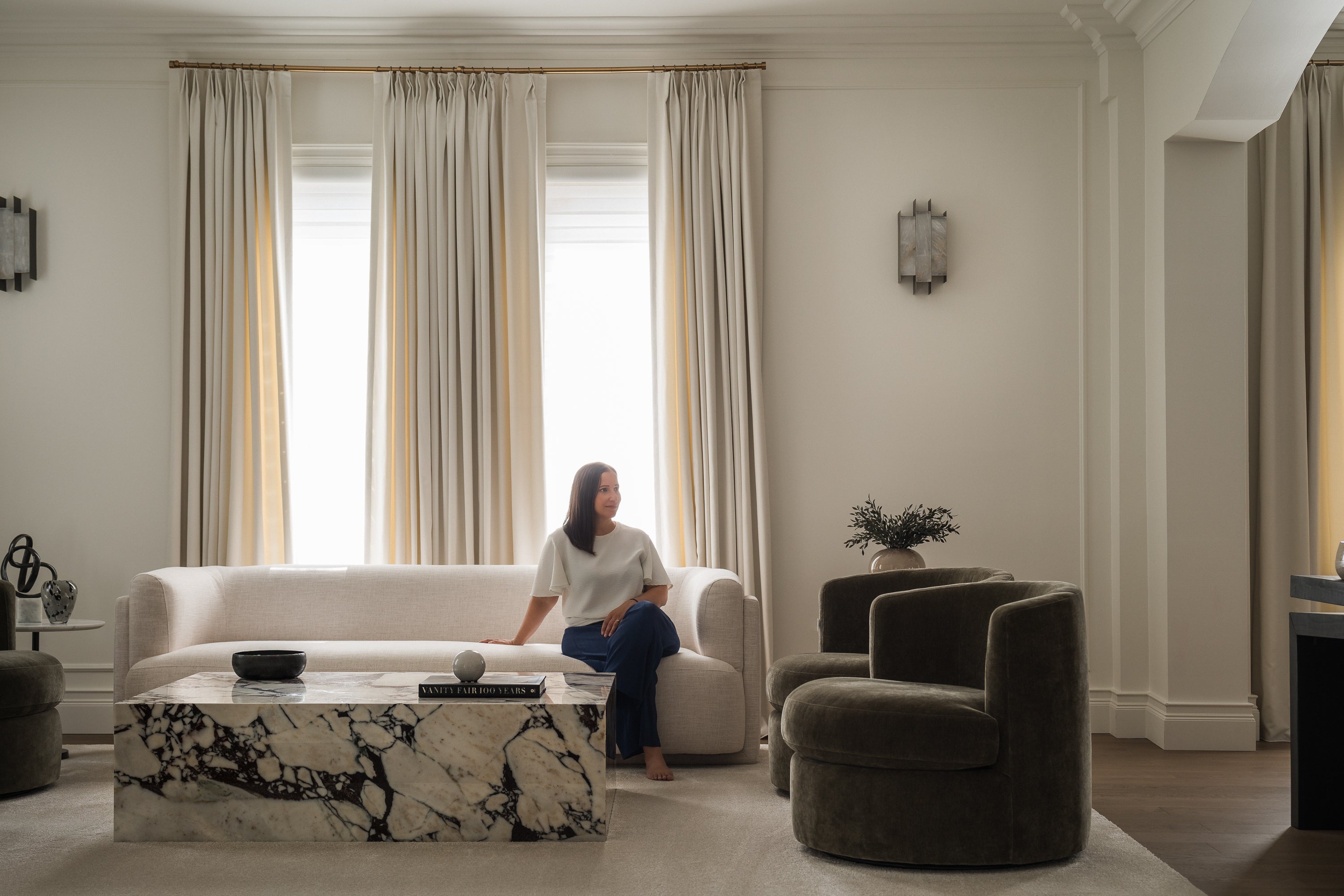 Photo of Melissa Kanfi, Interior Designer and Owner of Olive & Neon and Maison Juniper. Photo of formal living room with curved sofa and chairs, marble table and custom drapery.